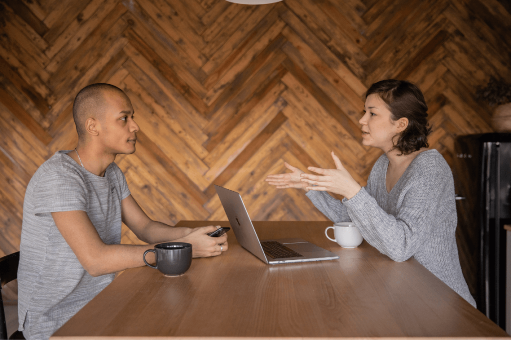 Two professionals sitting across from each other at a small table in a quiet office setting, engaged in a focused conversation. An open notebook and coffee cups sit between them as they maintain eye contact and relaxed posture, reflecting the supportive and thoughtful nature of business coaching built on listening, structured thinking, and collaborative decision-making rather than giving quick advice.