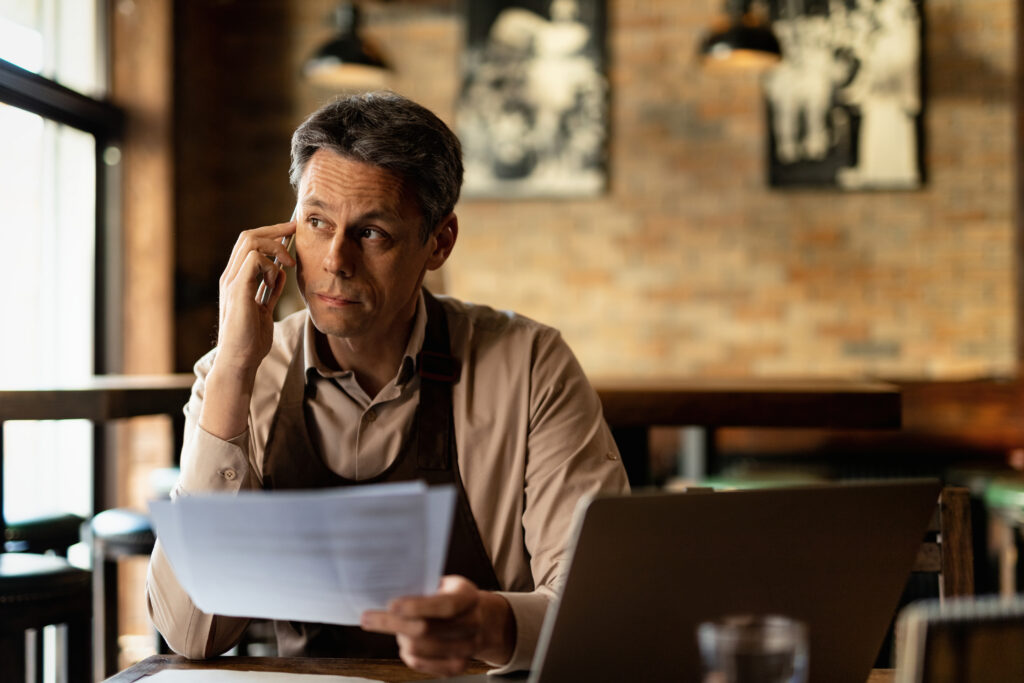 Small business owner reviewing documents and speaking on the phone, applying systems thinking for small business to daily operations