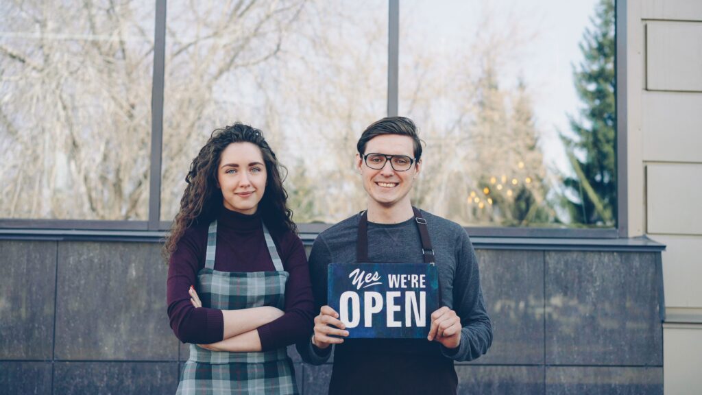 Economic Development Coaching for Small Business Owners Economic development coaching for small business owners, represented by two entrepreneurs standing outside their business with an open sign.