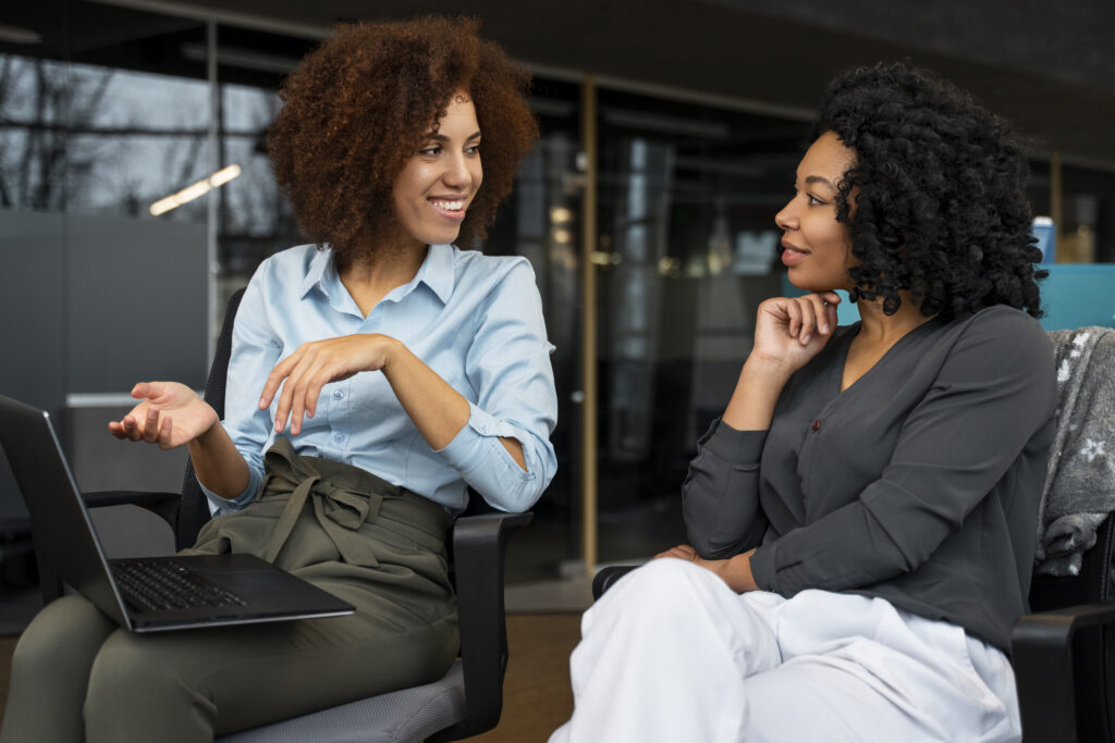 Business coach listening to a small business owner during a one-on-one coaching conversation with a laptop nearby, representing small business coaching certification, certified small business coach, appreciative inquiry business coaching, coach approach for consultants, and small business coaching tools