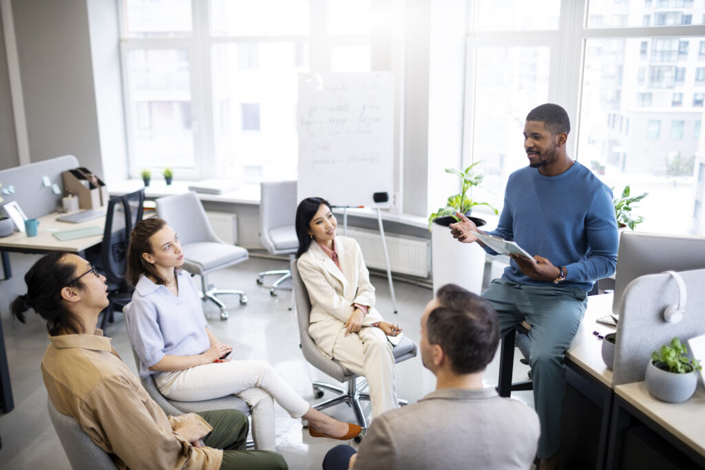 Medium shot of diverse professionals learning at work during a small business coach training session, with a business coach leading a team meeting focused on leadership, collaboration, and coach training for small business owners.