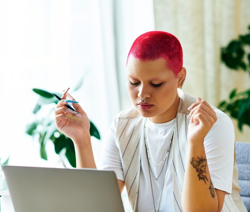 Woman holding a pen and thinking at a laptop, representing planning a focused next step